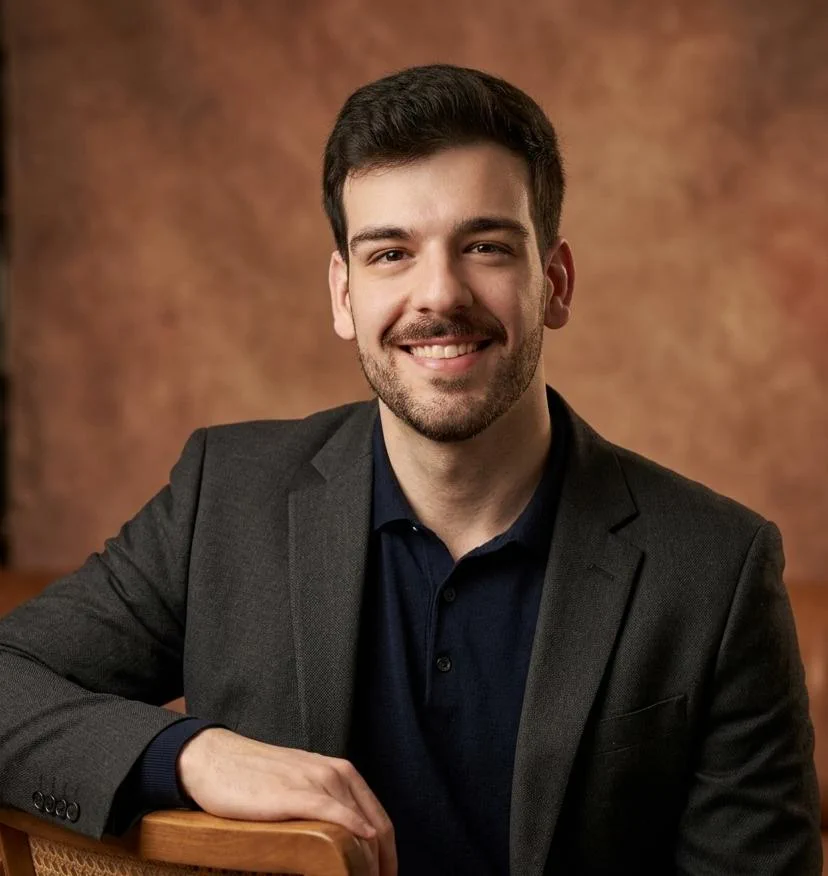Dr. Alvaro Frigini sorrindo, de blazer escuro, apoiado no encosto de uma cadeira.